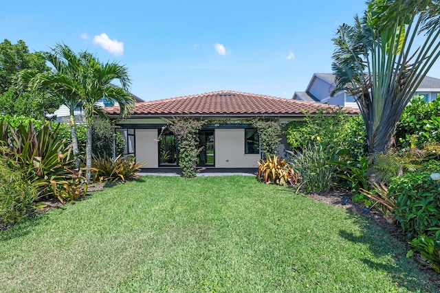 back of house featuring a tiled roof, a yard, and stucco siding