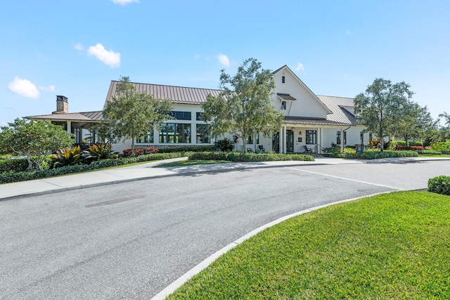 view of front of home featuring uncovered parking, a standing seam roof, metal roof, and a chimney