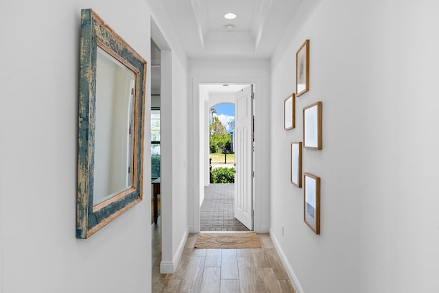 doorway to outside with baseboards, ornamental molding, a raised ceiling, and light wood-style floors