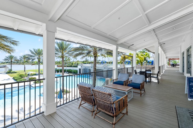 wooden deck with a community pool, fence, a water view, and outdoor dining area