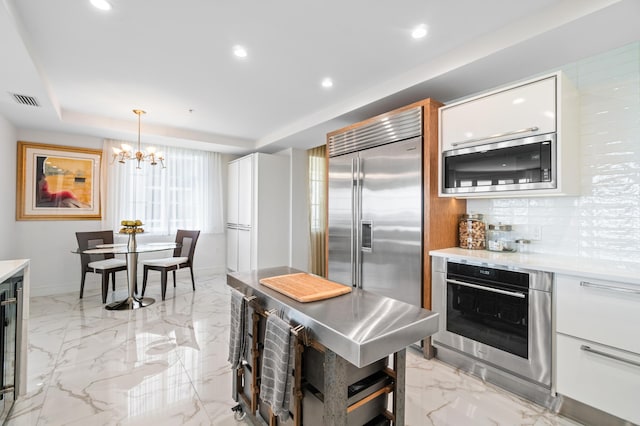 kitchen with built in appliances, white cabinets, light countertops, recessed lighting, and a chandelier