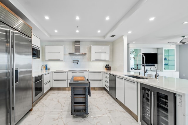 kitchen featuring built in appliances, wall chimney range hood, a sink, modern cabinets, and decorative backsplash