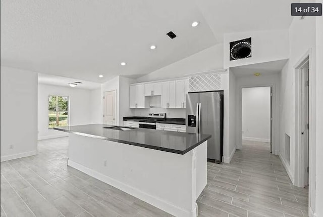 kitchen with white cabinets, dark countertops, a kitchen island with sink, stainless steel appliances, and baseboards