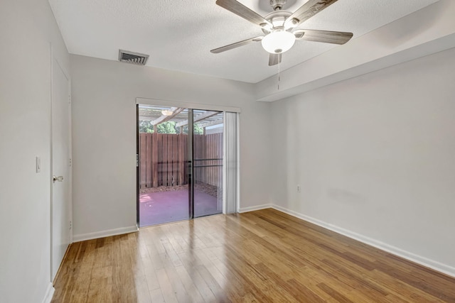 empty room with baseboards, a textured ceiling, wood finished floors, and visible vents