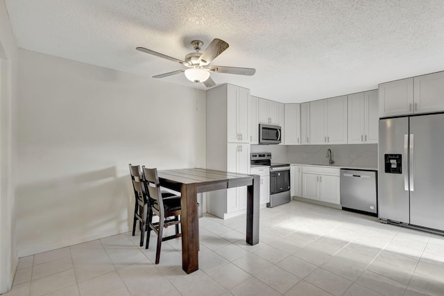 kitchen with ceiling fan, a textured ceiling, a sink, light tile patterned floors, and stainless steel appliances