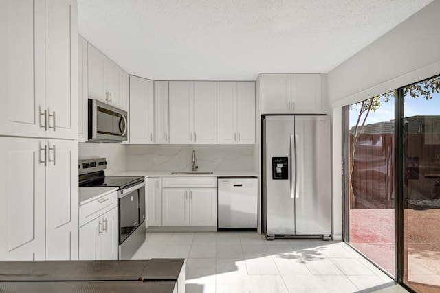 kitchen featuring light countertops, a textured ceiling, a sink, light tile patterned floors, and stainless steel appliances