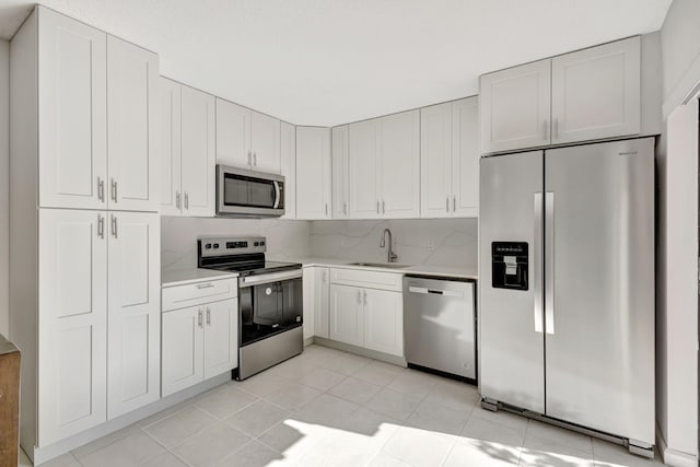 kitchen with a sink, light countertops, light tile patterned flooring, stainless steel appliances, and white cabinetry