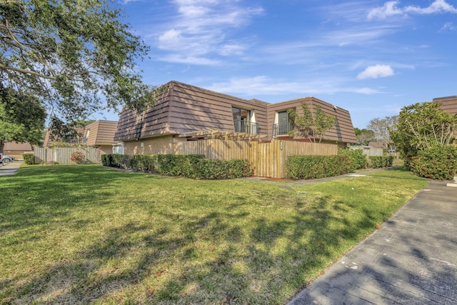 view of property exterior featuring a lawn, mansard roof, and fence