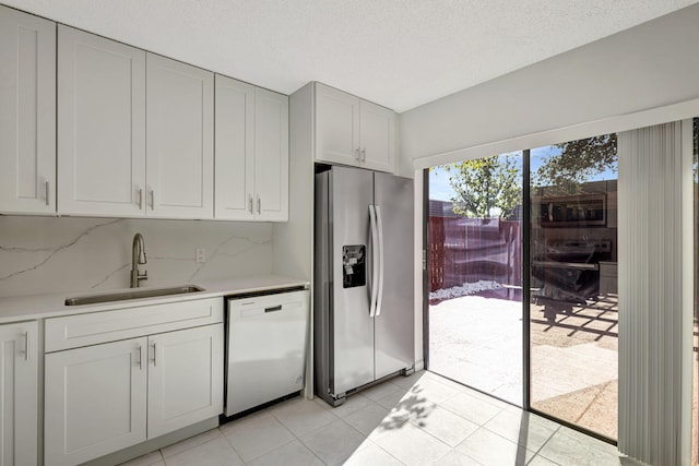 kitchen with light tile patterned flooring, stainless steel fridge, a sink, dishwasher, and light countertops