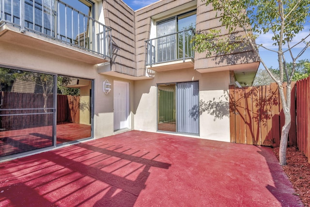 exterior space with a patio area, mansard roof, fence, a balcony, and stucco siding