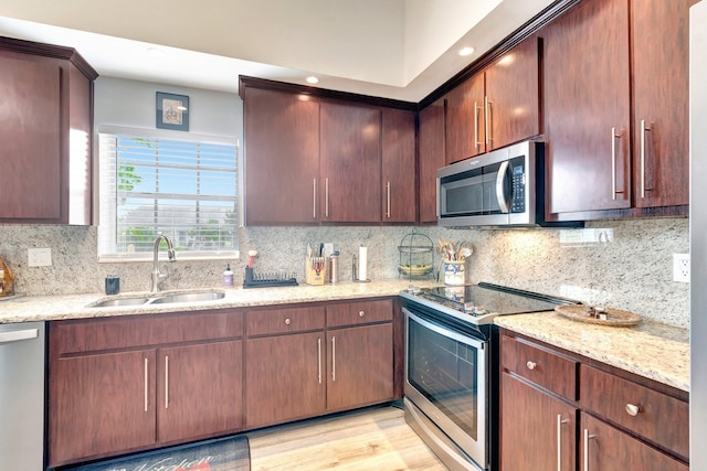 kitchen with a sink, backsplash, light stone countertops, and stainless steel appliances