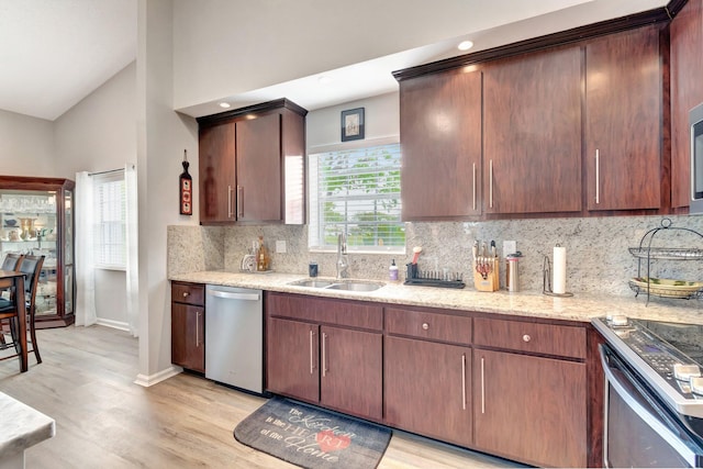 kitchen with light stone counters, appliances with stainless steel finishes, a sink, light wood-style floors, and backsplash