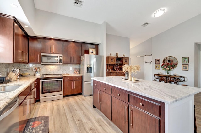 kitchen featuring backsplash, visible vents, light stone counters, light wood-style floors, and stainless steel appliances