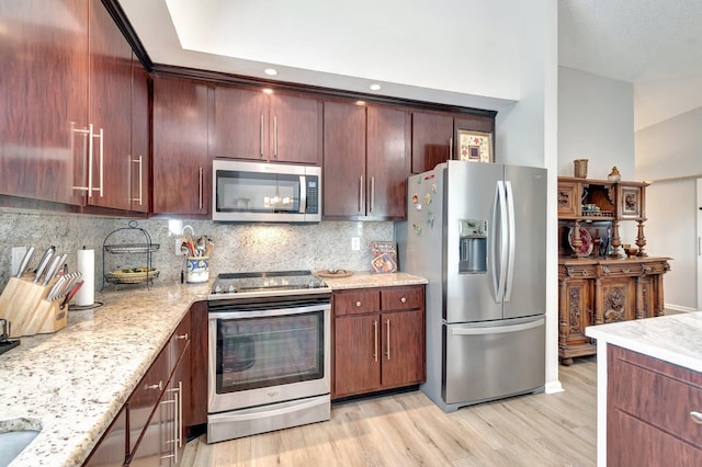kitchen featuring light stone countertops, appliances with stainless steel finishes, decorative backsplash, and light wood-style floors