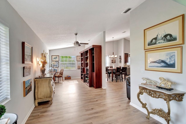 corridor with an inviting chandelier, light wood-style floors, baseboards, lofted ceiling, and visible vents