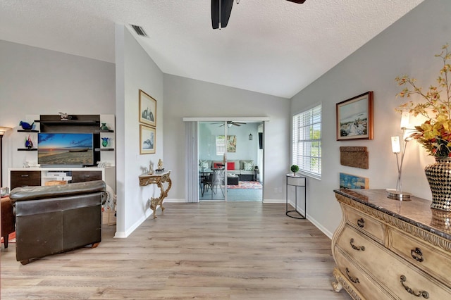 hallway with a textured ceiling, visible vents, vaulted ceiling, baseboards, and light wood-style floors