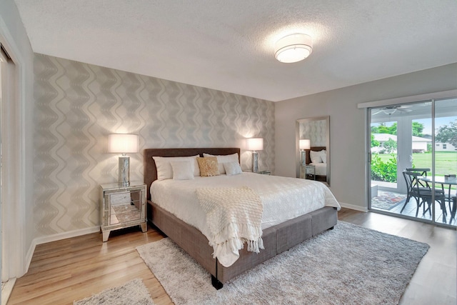 bedroom with baseboards, a textured ceiling, wood finished floors, and access to exterior