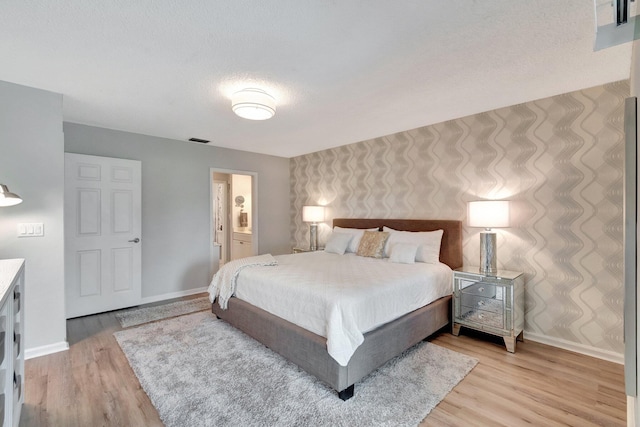bedroom with baseboards, visible vents, light wood-style flooring, and ensuite bath