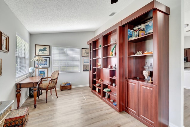 office with a textured ceiling, visible vents, lofted ceiling, and light wood finished floors