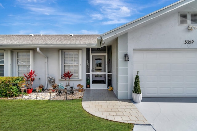 entrance to property featuring an attached garage, roof with shingles, stucco siding, a lawn, and driveway