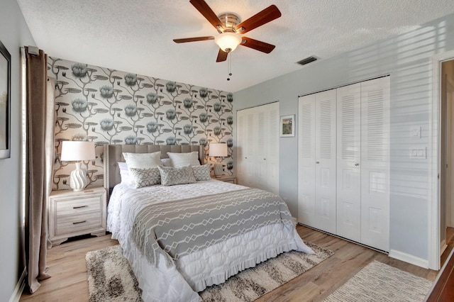 bedroom featuring a textured ceiling, visible vents, baseboards, light wood finished floors, and multiple closets