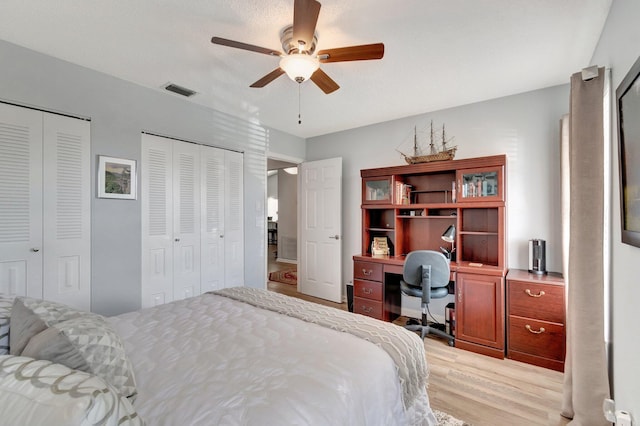 bedroom with light wood-type flooring, ceiling fan, two closets, and visible vents