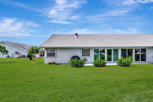 back of house featuring a yard, a shingled roof, and stucco siding