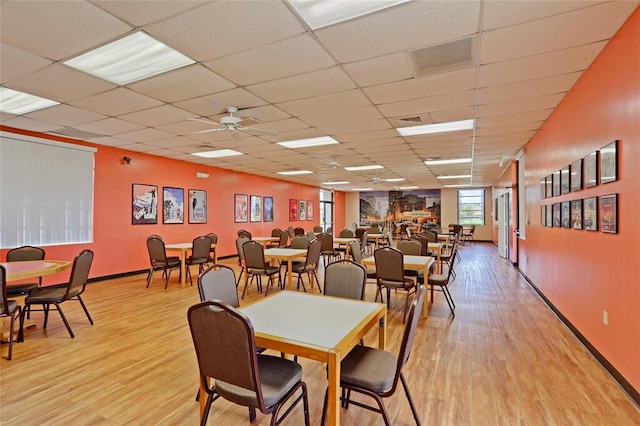 dining space with baseboards, light wood-style flooring, ceiling fan, and a drop ceiling
