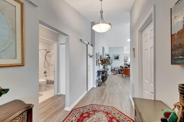 hallway with baseboards, visible vents, a barn door, and light wood-style floors