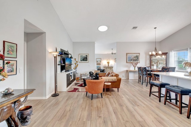 living room featuring ceiling fan with notable chandelier, vaulted ceiling, light wood finished floors, and visible vents