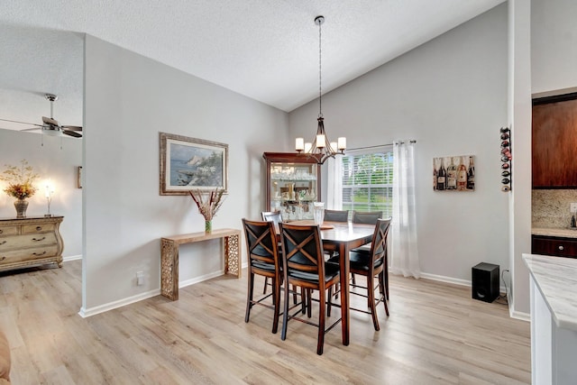 dining space featuring baseboards, high vaulted ceiling, a textured ceiling, light wood-style flooring, and ceiling fan with notable chandelier