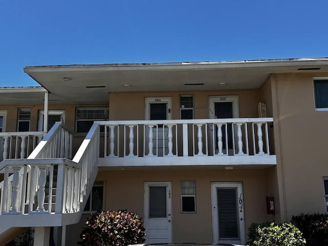 back of house with stucco siding, a balcony, and stairs