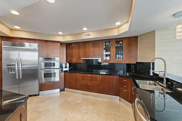 kitchen featuring glass insert cabinets, a sink, stainless steel appliances, brown cabinetry, and visible vents