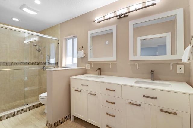full bath featuring toilet, a stall shower, double vanity, and recessed lighting