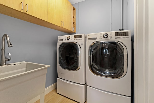 clothes washing area featuring cabinet space, washer and dryer, light wood-style floors, and baseboards