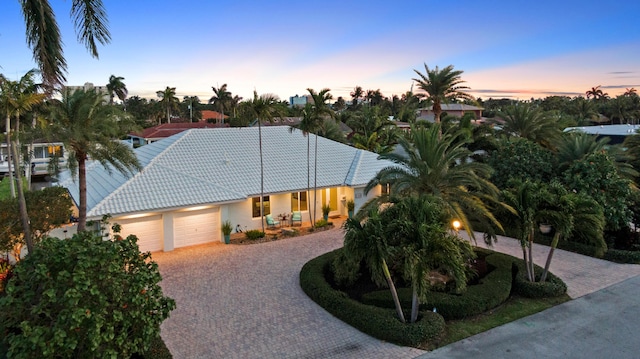 ranch-style home featuring decorative driveway, a tiled roof, an attached garage, and stucco siding