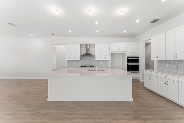 10241 SW Carnelian St, Port Saint Lucie, FL 34987 - kitchen featuring visible vents, a kitchen island with sink, light countertops, wall chimney exhaust hood, and backsplash