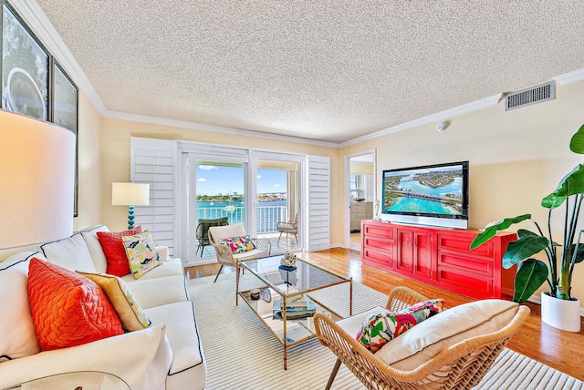 living area featuring ornamental molding, visible vents, a textured ceiling, and wood finished floors
