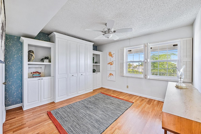 unfurnished bedroom with baseboards, light wood finished floors, wallpapered walls, and a textured ceiling