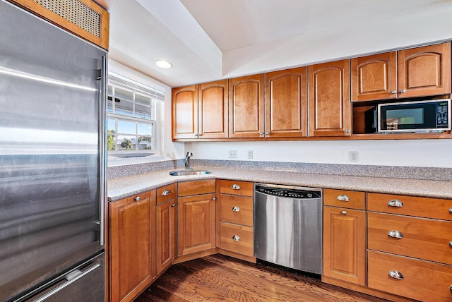 kitchen featuring appliances with stainless steel finishes, dark wood-type flooring, brown cabinets, and a sink