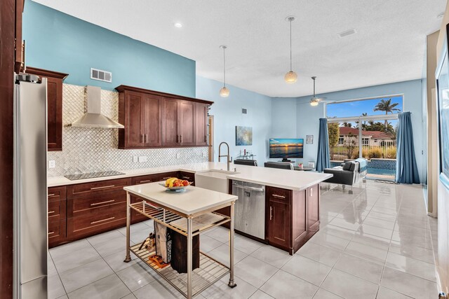 kitchen featuring a sink, wall chimney exhaust hood, stainless steel appliances, a peninsula, and visible vents