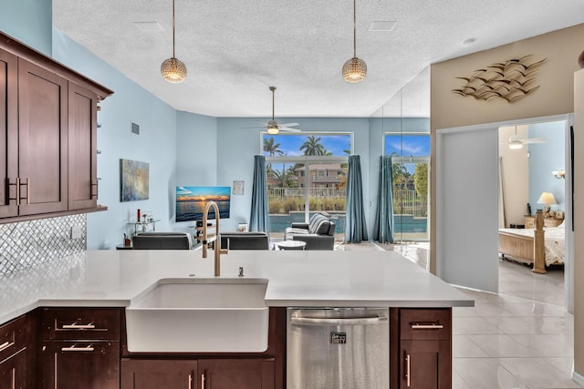 kitchen with stainless steel dishwasher, a ceiling fan, a textured ceiling, a sink, and hanging light fixtures