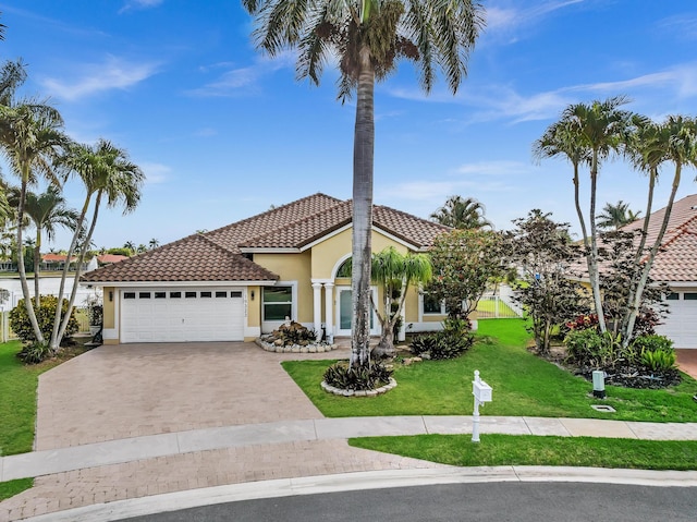 mediterranean / spanish house featuring decorative driveway, a garage, stucco siding, and a tiled roof