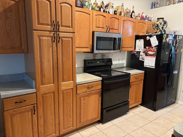 kitchen featuring brown cabinetry, light countertops, light tile patterned flooring, and black appliances