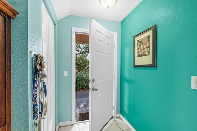 foyer featuring baseboards, vaulted ceiling, and light tile patterned floors