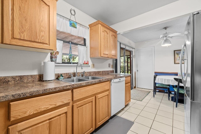 kitchen featuring white dishwasher, light tile patterned flooring, dark countertops, a sink, and freestanding refrigerator