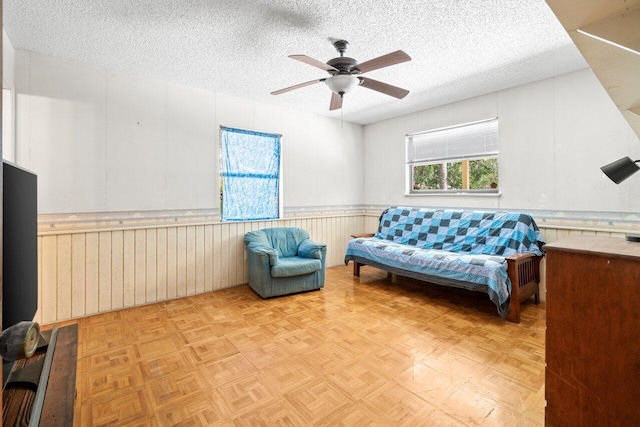 sitting room with a wainscoted wall, a ceiling fan, and a textured ceiling