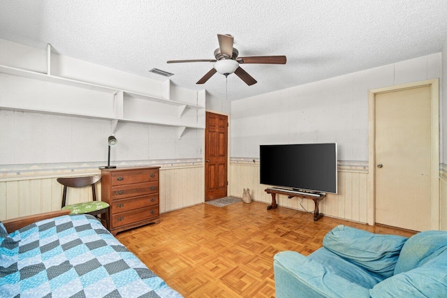 bedroom with a wainscoted wall, a ceiling fan, a textured ceiling, and visible vents