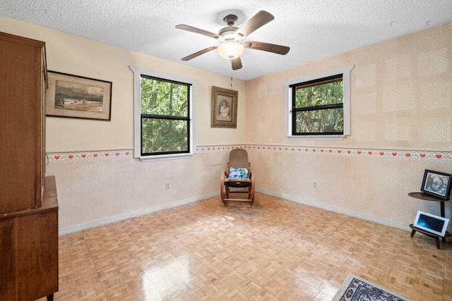 unfurnished room with a wainscoted wall, ceiling fan, baseboards, and a textured ceiling