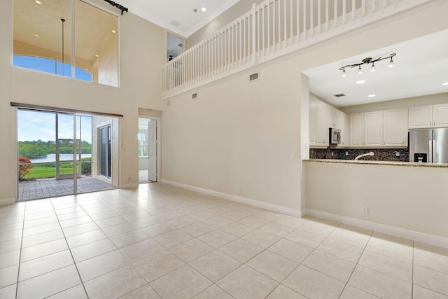 unfurnished living room featuring baseboards, visible vents, light tile patterned floors, and a towering ceiling